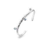 A close-up shot of a chunky sterling silver bangle with a textured surface, similar to a rock, on a white background. Three light blue topaz stones are inlaid into the bangle. The bangle is open at the back.
